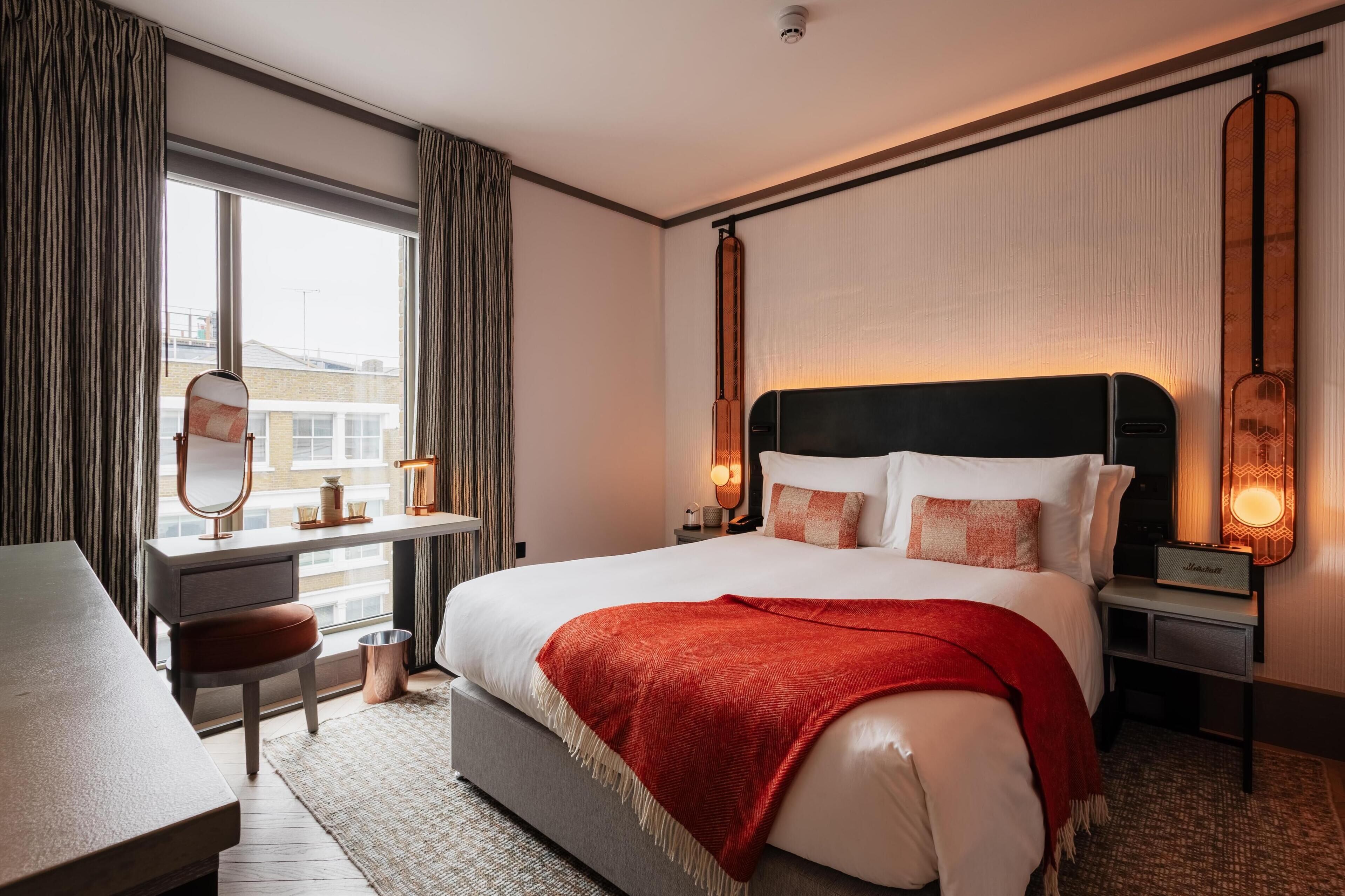 Une chambre d’hôtel moderne avec un grand lit, un bureau et une vue sur les bâtiments à l’extérieur de la fenêtre.
