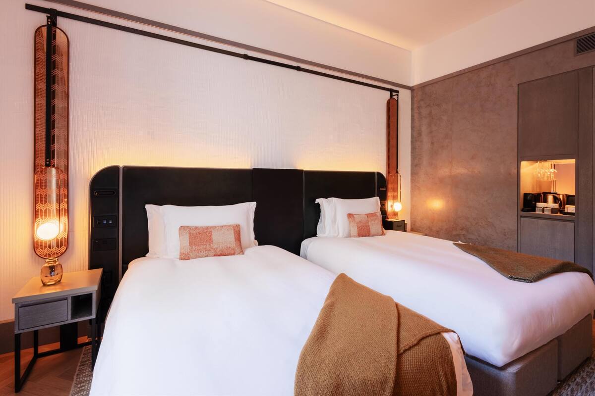 A hotel room with two beds, a nightstand with a lamp, and a wardrobe.