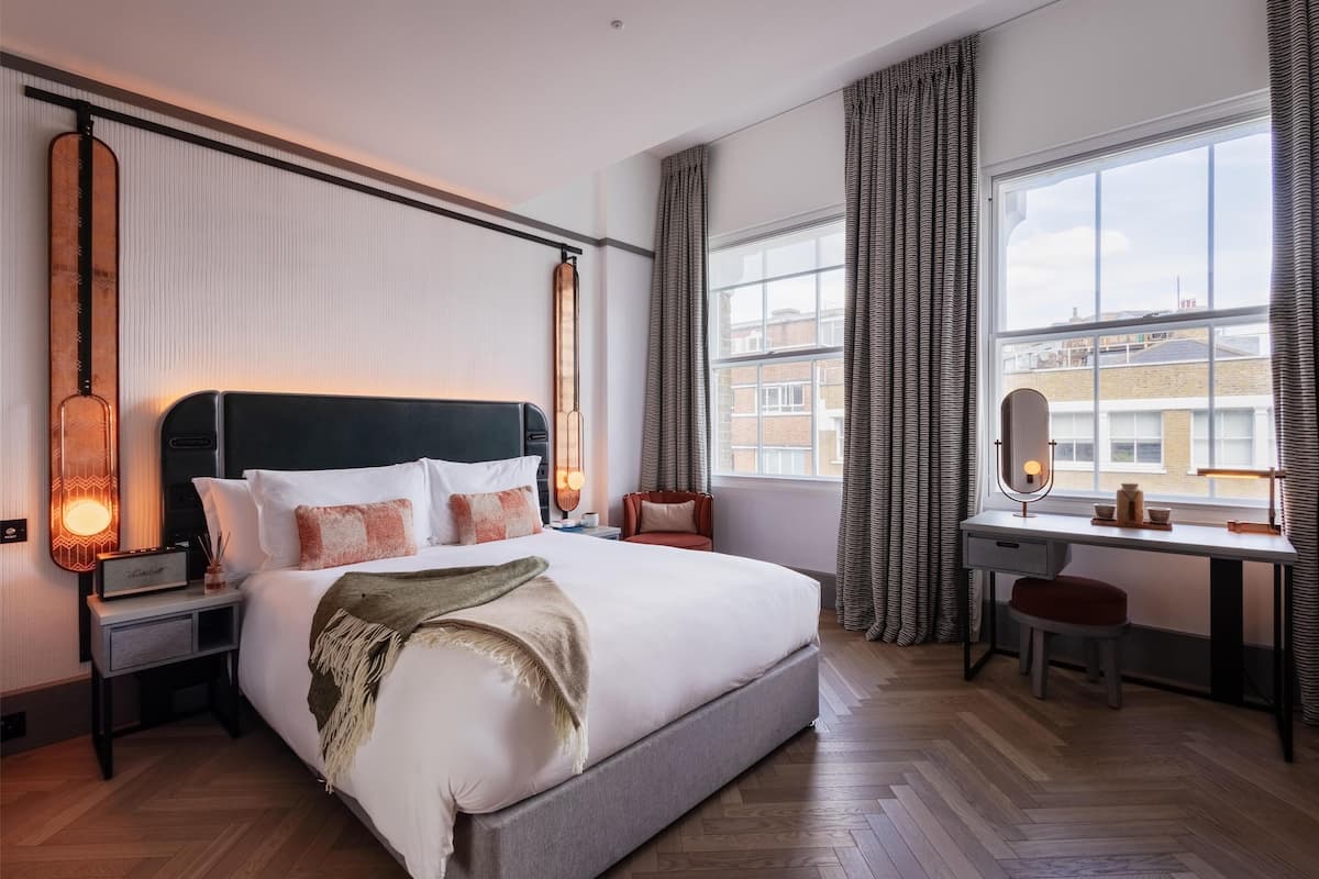A hotel room with a large bed, bedside tables, a desk, and a window with curtains.