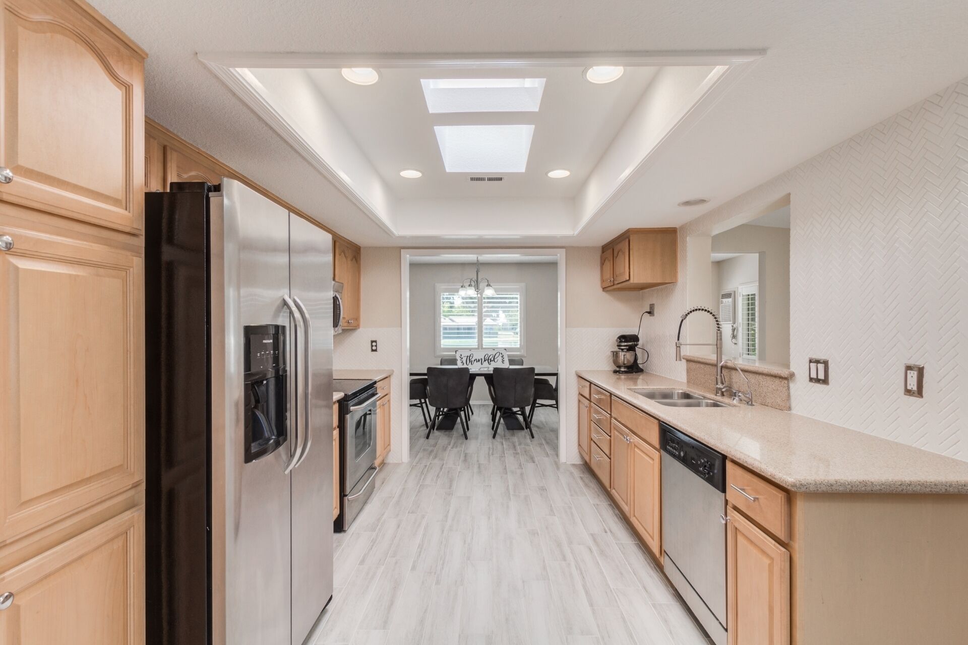 A modern kitchen with wooden cabinets, a stainless steel refrigerator, a dishwasher, and a dining area with a table and chairs.