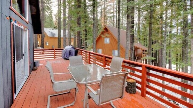 A wooden deck with a table and chairs, surrounded by a red railing, overlooking a forested area. - Scenic Wonders Christmas Cabin 3 Bedroom (Yosemite National Park)