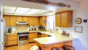A compact kitchen with wooden cabinets, a built-in oven, a dishwasher, and a large island with a sink. - Scenic Wonders Christmas Cabin 3 Bedroom (Yosemite National Park)