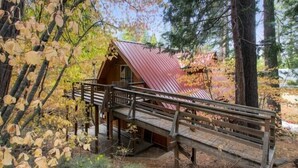 A cabin with a wooden deck and a metal roof, surrounded by trees and a forested area. - Scenic Wonders Clark Cabin 3 Bedrooms (Yosemite National Park)