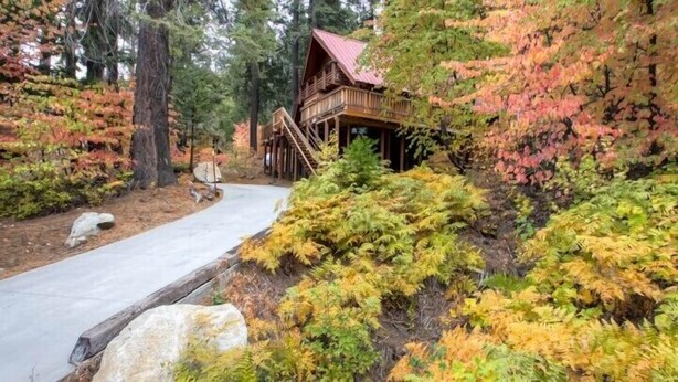 A wooden cabin with a red roof, surrounded by autumn-colored trees and a paved path leading to it. - Scenic Wonders Clark Cabin 3 Bedrooms (Yosemite National Park)