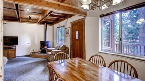 A cozy room with a fireplace, wooden furniture, and large windows offering a view of the outdoors. - Scenic Wonders Clark Cabin 3 Bedrooms (Yosemite National Park)