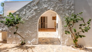 Un arc en pierre mène à l’entrée d’un bâtiment, qui donne sur un patio carrelé et offre une vue sur l’intérieur.