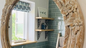 Un miroir décoratif reflétant une salle de bain aux carreaux turquoise, une fenêtre et des étagères décoratives.