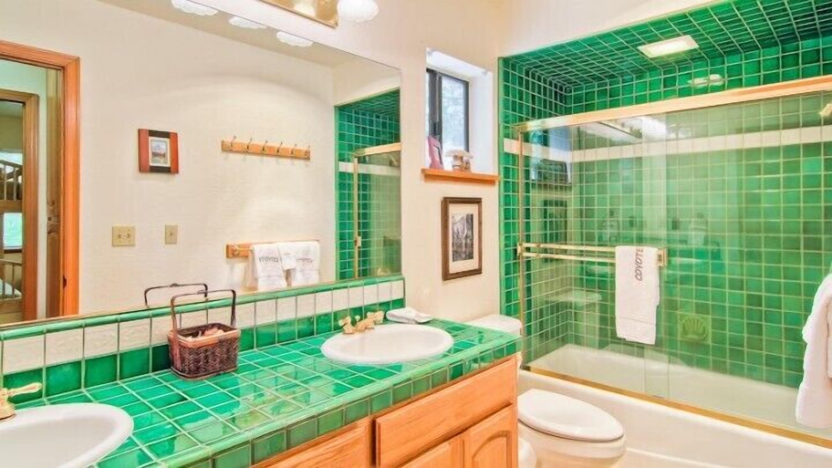 Um banheiro com azulejos verdes, pia, vaso sanitário e área de chuveiro.