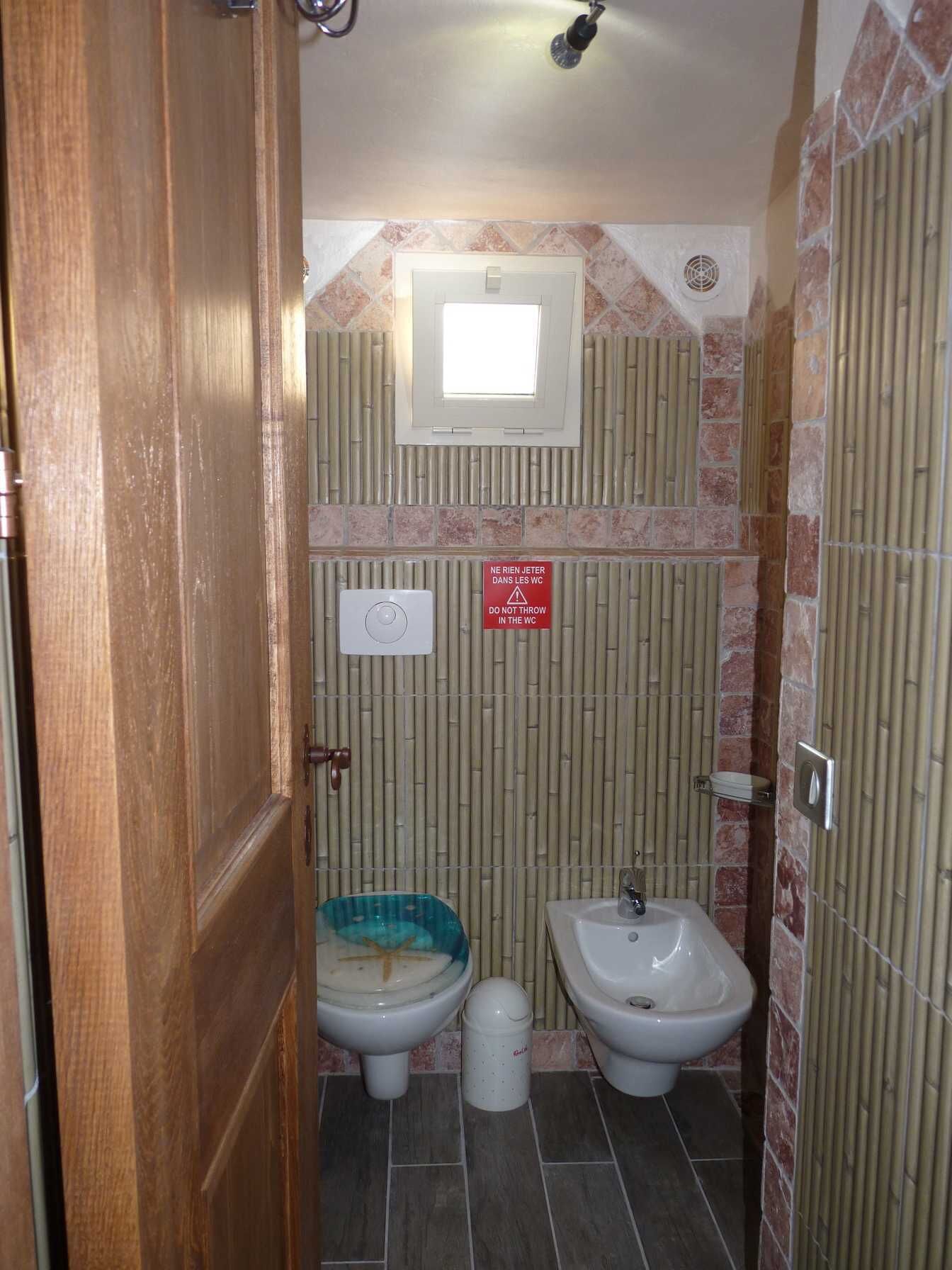 Ein kleines Badezimmer mit zwei Toiletten, einem Waschbecken und einem Fenster.