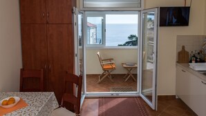 Une cuisine donnant sur la mer, une table à manger avec un saladier de fruits et un téléviseur fixé au mur.