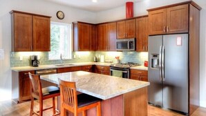 A modern kitchen with wooden cabinets, a stainless steel refrigerator, a microwave, and a large island with bar stools.