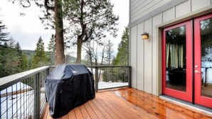 A wooden deck with a barbecue grill, a red door, and a view of trees and hills.