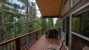 Une terrasse en bois dotée d’un espace salon abrité, entourée de grands arbres.