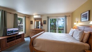 Une chambre à coucher avec un grand lit, un téléviseur posé sur un meuble en bois, une commode et une fenêtre avec des rideaux.