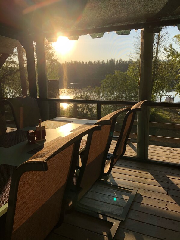 Een houten terras met een tafel en stoelen, met uitzicht op water en bomen.
