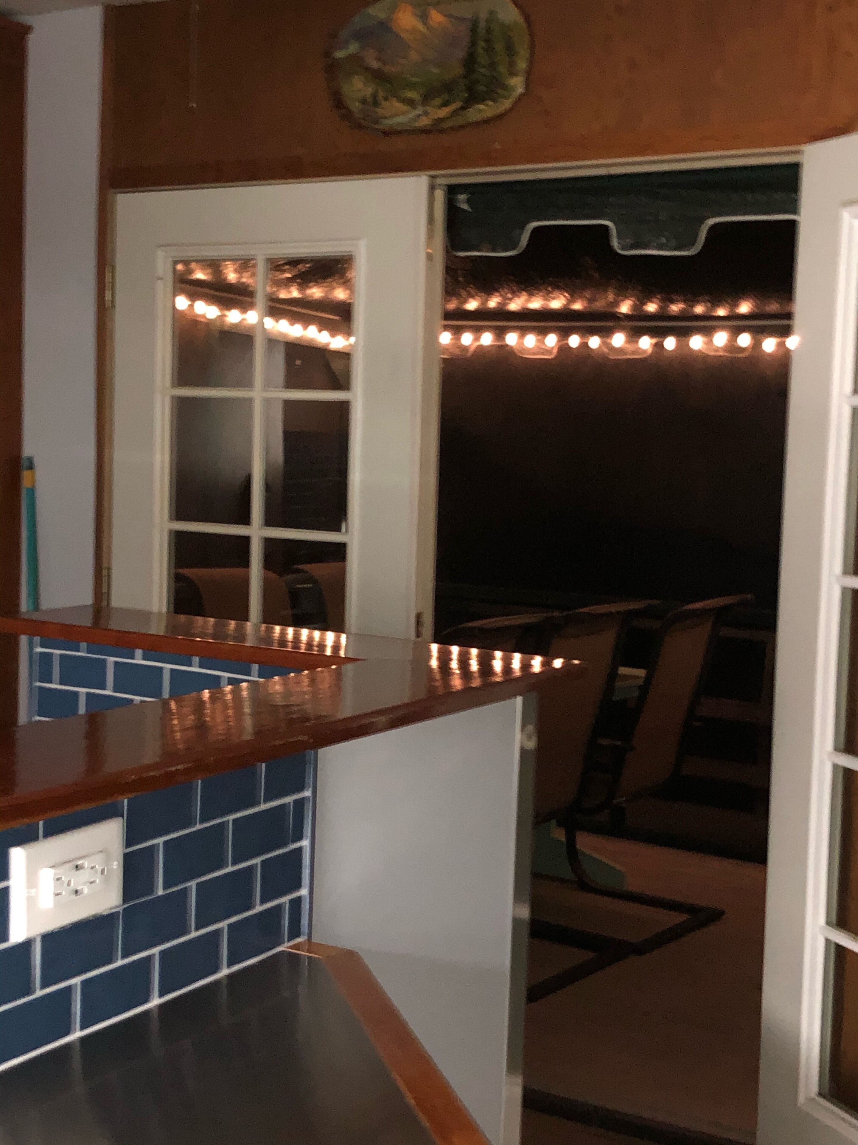 Une cuisine dotée d’un plan de travail en bois, d’un pare-feu en carrelage et d’une porte donnant sur un balcon illuminé de guirlandes lumineuses.