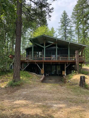A cabin with a covered deck and a large window overlooking a forested area. - Papa's Place - A secluded lake front property on the edge of Whitefish (Whitefish)