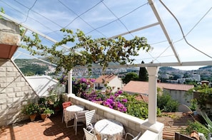Una terraza con vistas a un paisaje urbano, que incluye una pérgola, plantas en macetas y mobiliario exterior.