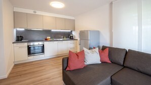 Una cocina moderna con electrodomésticos integrados, suelo de madera y un sofá gris con cojines rojos.
