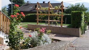 Un jardín con un enrejado de madera, un banco de concreto y un sendero.