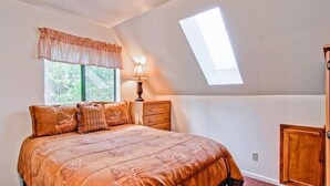 A bedroom with a bed, a nightstand, a lamp, a window with a view of trees, and a skylight. - Scenic Wonder Pinetree Retreat 3 Bedroom (Yosemite National Park)