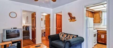 Un espacio habitable compacto con sofá, televisión, mesa de madera y ventilador de techo.