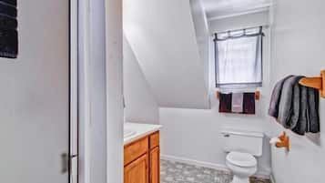Uma casa de banho pequena e estreita, com sanita, janela e um porta-toalhas.