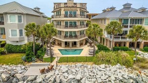 A multi-story residential building with a swimming pool, surrounded by palm trees and a rocky landscape. - First Floor, Oceanfront Condo, Concierge Service! (Saint Simons Island)