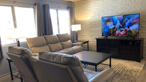 A modern living room with a reclining sofa, a coffee table, a TV on a stand, and a lamp. - Cntrl Tucson Home, Salt Water Pool, Hot Tub, Bike Path, 3mi to UofA TPT 20128463 (Tucson)