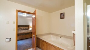 A bathroom with a wooden vanity, a large bathtub, and a door leading to a bedroom with a bed and a nightstand. - Scenic Wonders Quail Crossing 3 Bedrooms (Yosemite National Park)