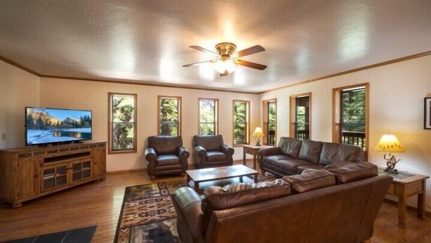 A spacious living room with a large leather sofa, two armchairs, a coffee table, a wooden entertainment unit, and a ceiling fan. - Scenic Wonders Quail Crossing 3 Bedrooms (Yosemite National Park)