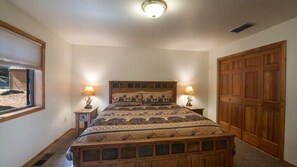 A bedroom with a wooden bed, two bedside lamps, a window with a view of a beach, and a wooden wardrobe. - Scenic Wonders Quail Crossing 3 Bedrooms (Yosemite National Park)
