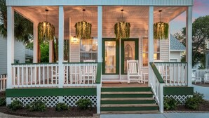 A porch with white railings, green steps, and hanging plants.