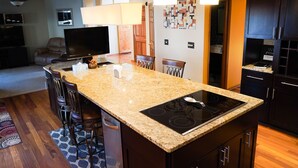 A kitchen with granite countertops, a built-in stove, bar stools, and a dining area with a TV.