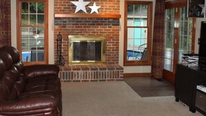 A living room with a fireplace, leather sofas, a ceiling fan, and brick walls.