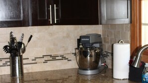 A kitchen with dark wooden cabinets, a granite countertop, a stand mixer, a paper towel holder, and a stainless steel sink.