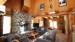 A log cabin interior with a stone fireplace, a television, and a billiards table.