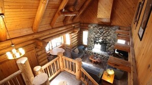 A log cabin interior with a stone fireplace, wooden furniture, and a wooden staircase.