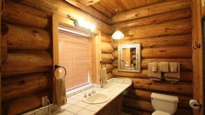 A log cabin bathroom with a wooden interior, a sink, a toilet, and a mirror. - Scenic Wonders Tioga Logs 3 Bedrooms (Yosemite National Park)