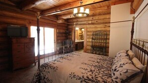 A log cabin bedroom with a bed, dresser, and a chandelier.