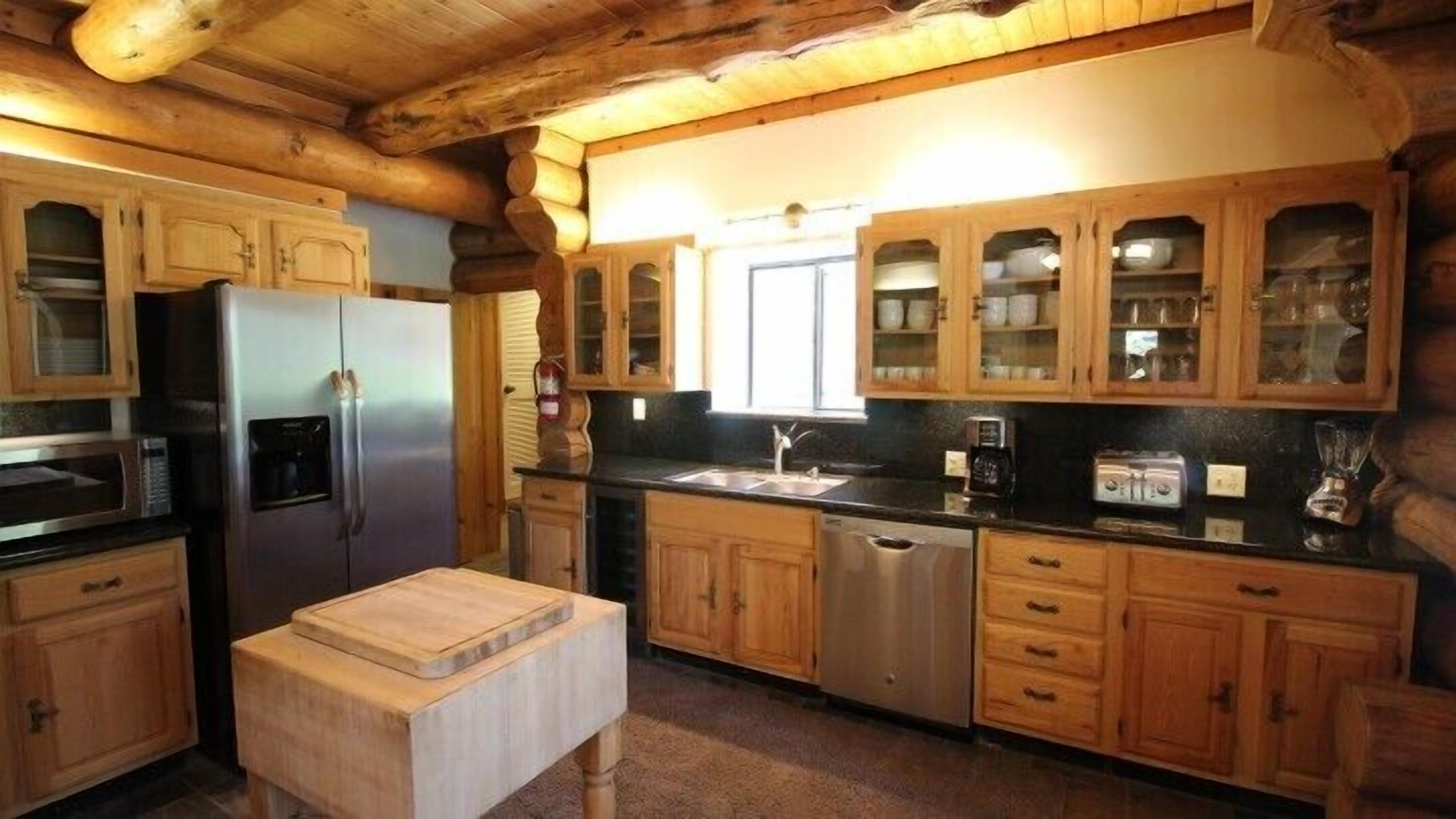 A log cabin kitchen with wooden cabinets, a stainless steel refrigerator, a sink, and a coffee maker.