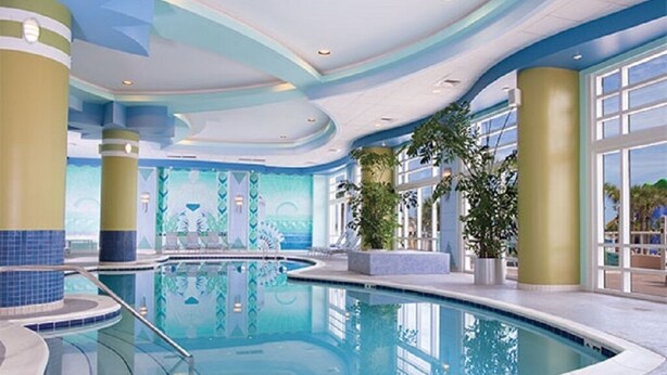 Una piscina interior con una decoración azul y blanca, rodeada de pilares imponentes y plantas en macetas.