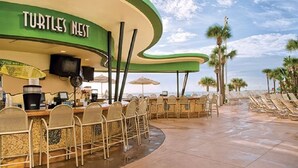 Un bar junto a la playa llamado 'Turtles Nest' con terraza al aire libre y palmeras al fondo.