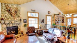 Una sala de estar acogedora con una pared de piedra, muebles de cuero, una chimenea y una estantería.