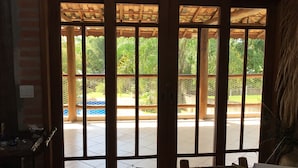 A wooden door with a view of a swimming pool and greenery outside. - CHÁCARA MARANATA - ATIBAIA | Rentals for Weekends, Holidays and Seasons. (ATIBAIA)