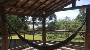 A hammock under a wooden pergola with a view of a green landscape and a body of water. - CHÁCARA MARANATA - ATIBAIA | Rentals for Weekends, Holidays and Seasons. (ATIBAIA)