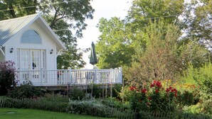 A white house with a balcony, surrounded by lush greenery and flowering plants. - Mallard Cottage - Pet friendly (Newfield)