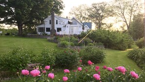 A white house with a stone chimney, surrounded by a well-maintained garden with pink flowers and a wooden fence. - Mallard Cottage - Pet friendly (Newfield)