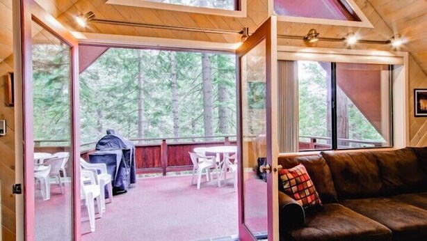 A cabin interior with a wooden ceiling, a brown leather sofa, and a view of a forest through large windows. - Scenic Wonders Yosemite Escape 3 Bedroom (Yosemite National Park)