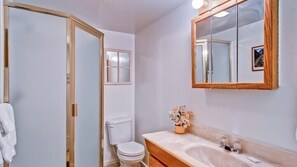 A bathroom with a wooden door, a white toilet, a sink with a mirror, and a small vase with flowers. - Scenic Wonders Yosemite Escape 3 Bedroom (Yosemite National Park)